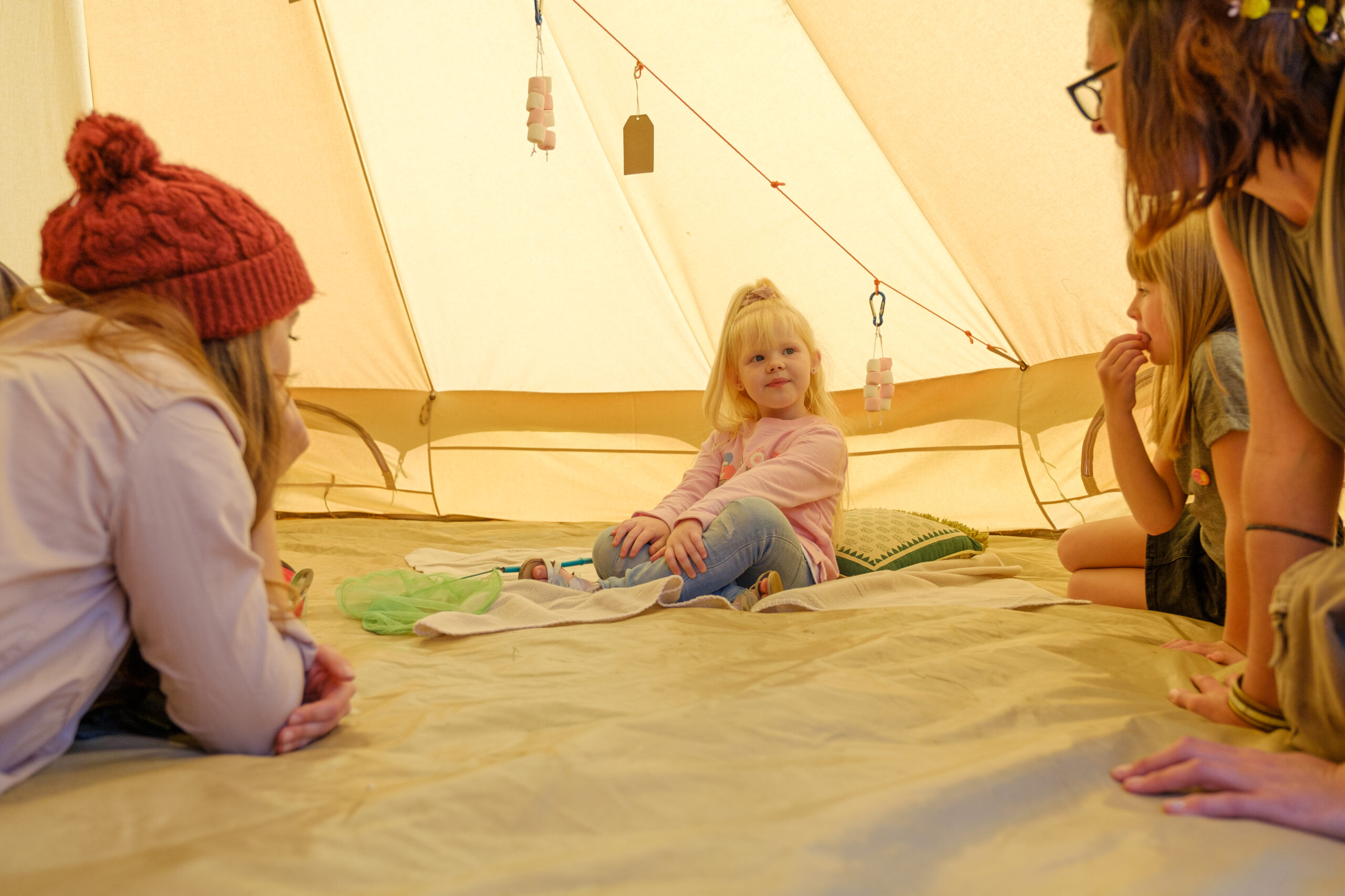 A small group of children and adults sit inside a tent